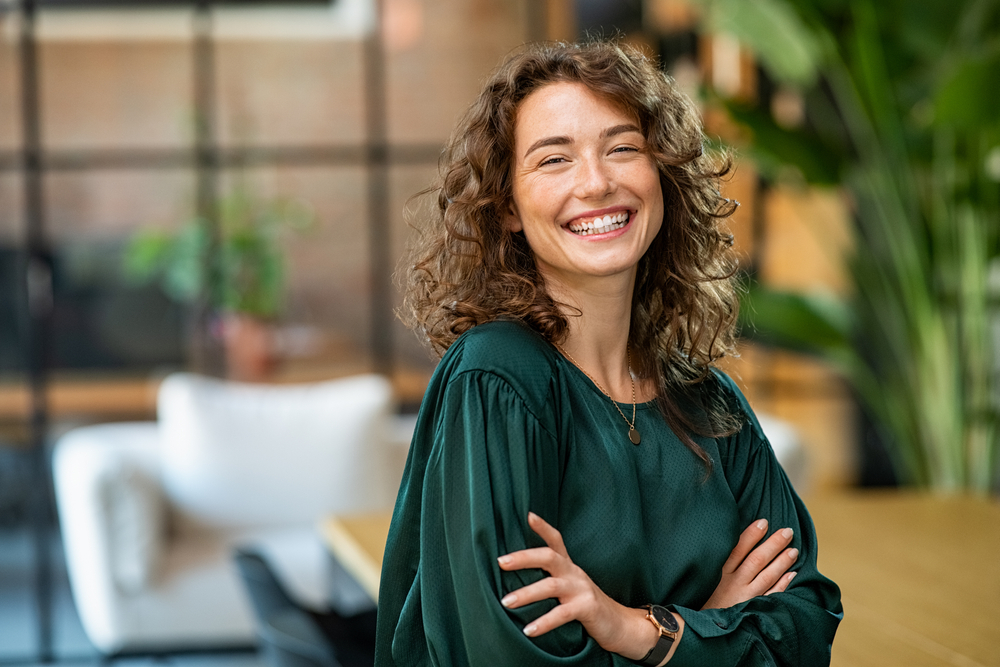 A woman smiling, arms folded, in a bright room