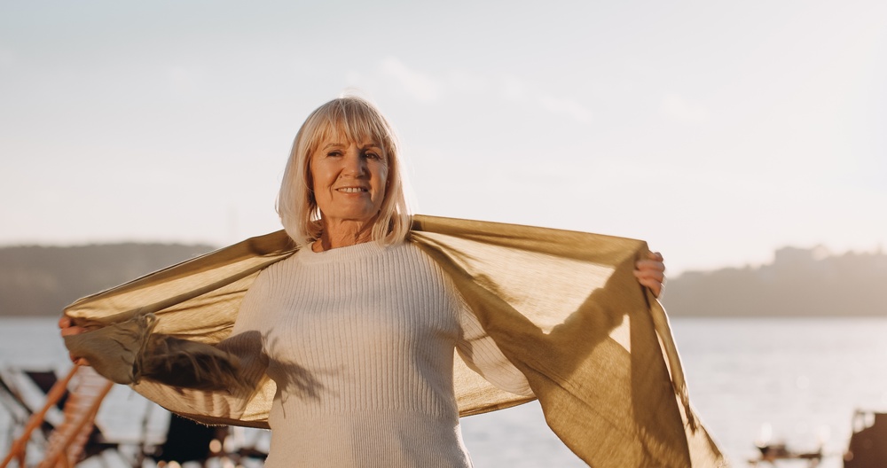 A woman in a scarf standing beside water, looking into the distance