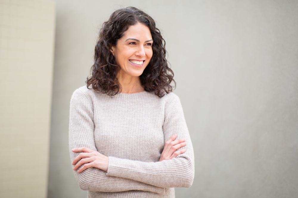 A woman with her arms folded, standing against a grey wall
