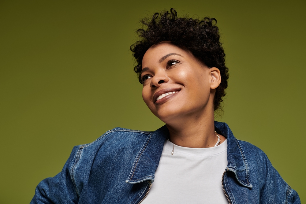 A woman in a denim jacket against an olive background, smiling