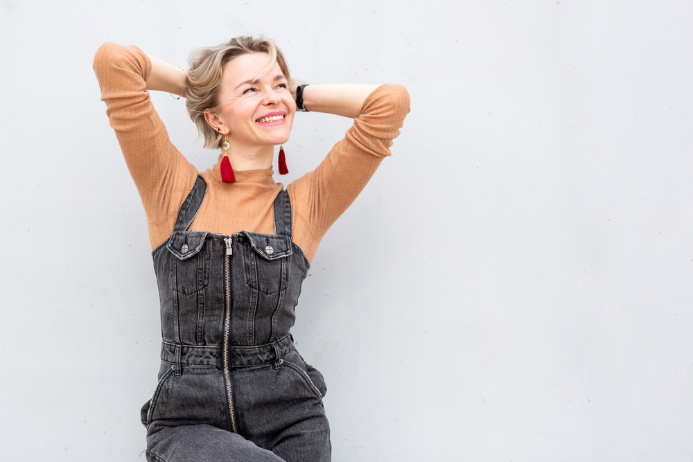 A woman smiling with her arms raised, against a pale wall