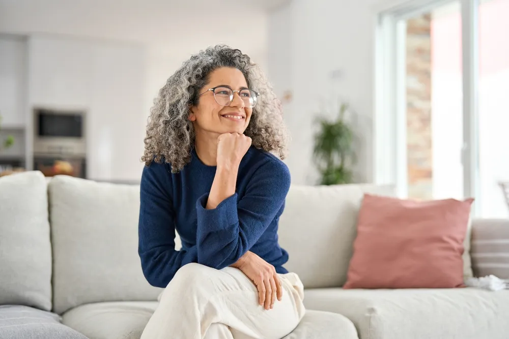 A woman with grey curls sitting on a sofa, smiling