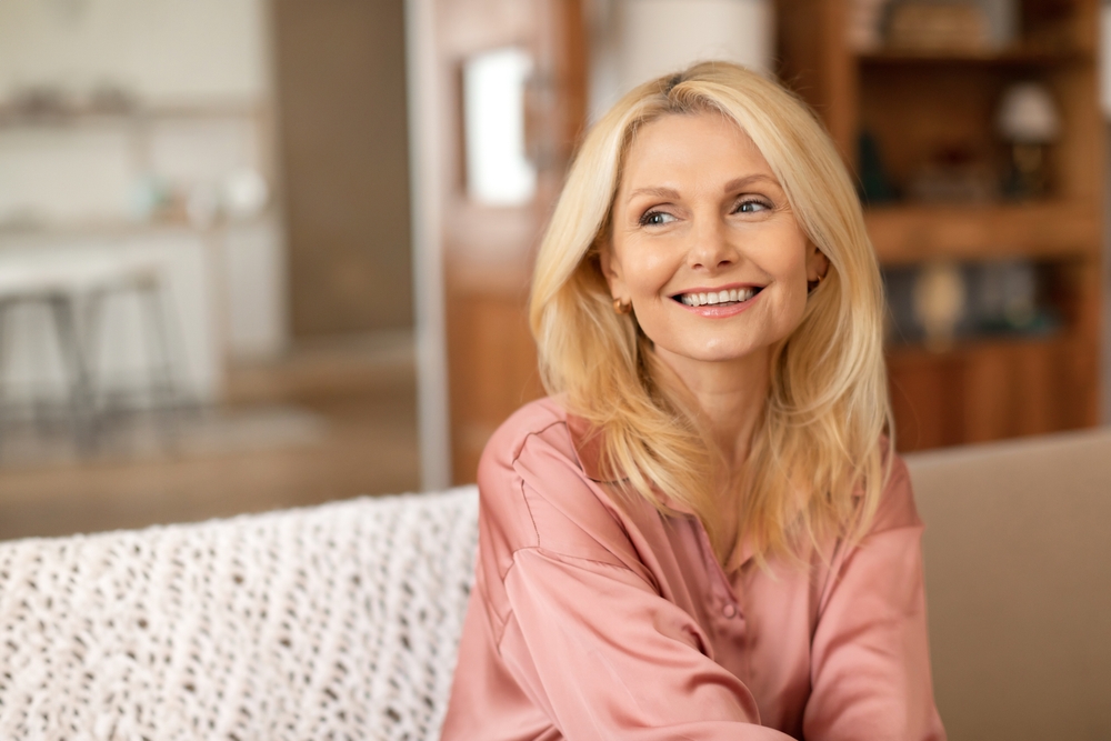 A woman in a pink blouse sitting on a sofa, smiling