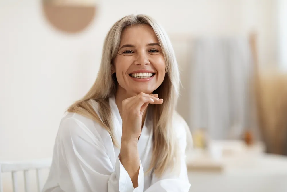 A woman in a white shirt in a bright room, smiling