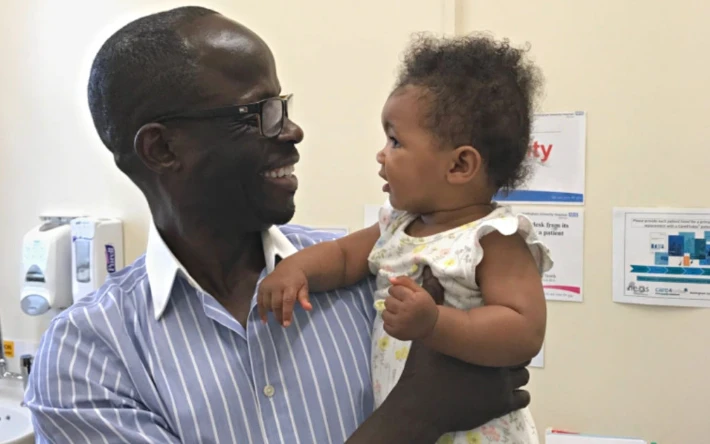 Mr Abu holding a patient's baby in clinic