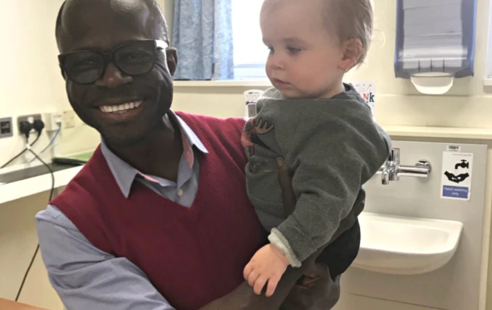 Mr Abu with a patient's toddler in clinic